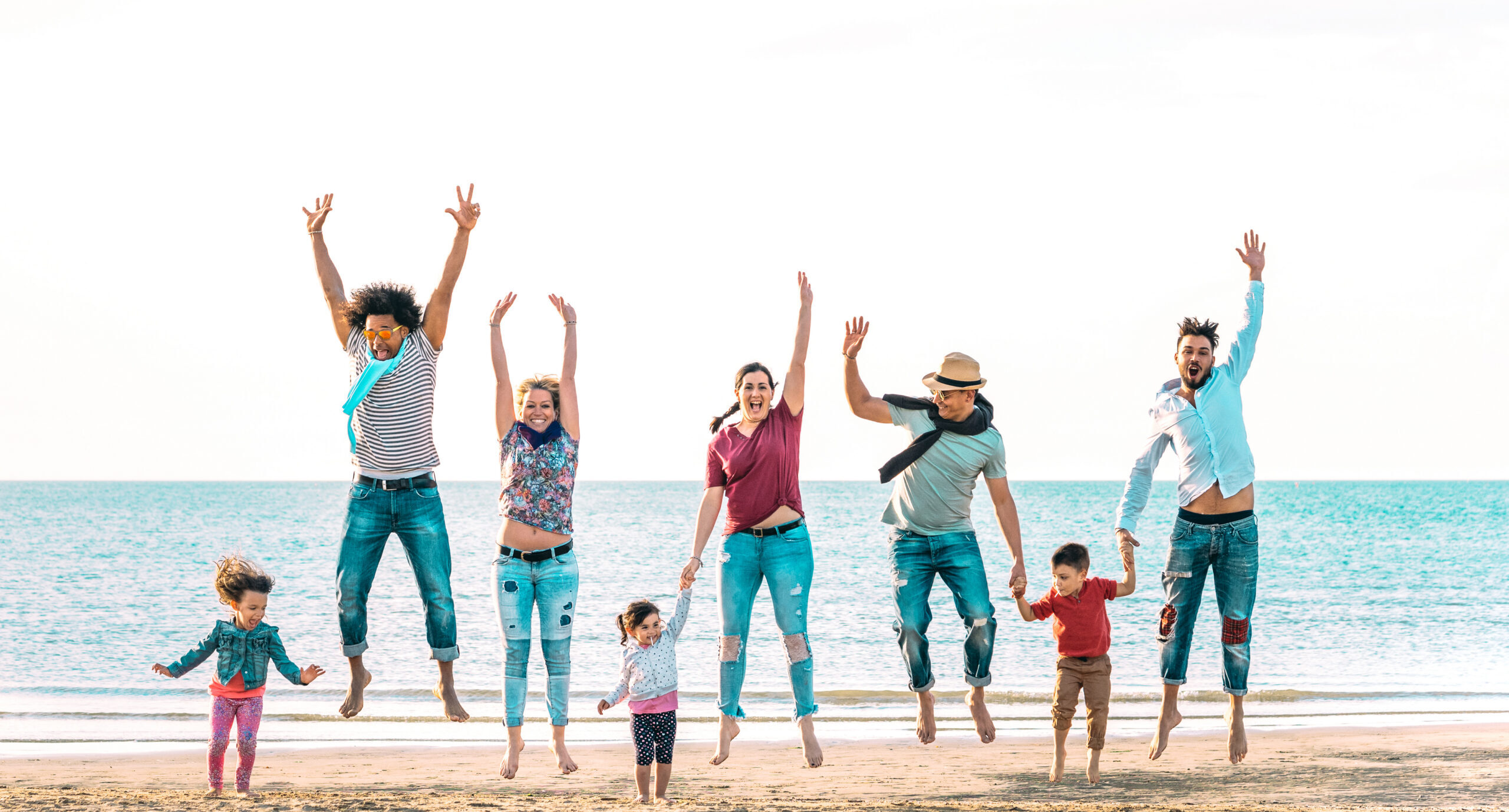 Happy multiracial families jumping together at beach holding hands - Summer vacation concept with young mixed race people having genuine fun outdoors enjoying sunset - Vivid azure backlight filter